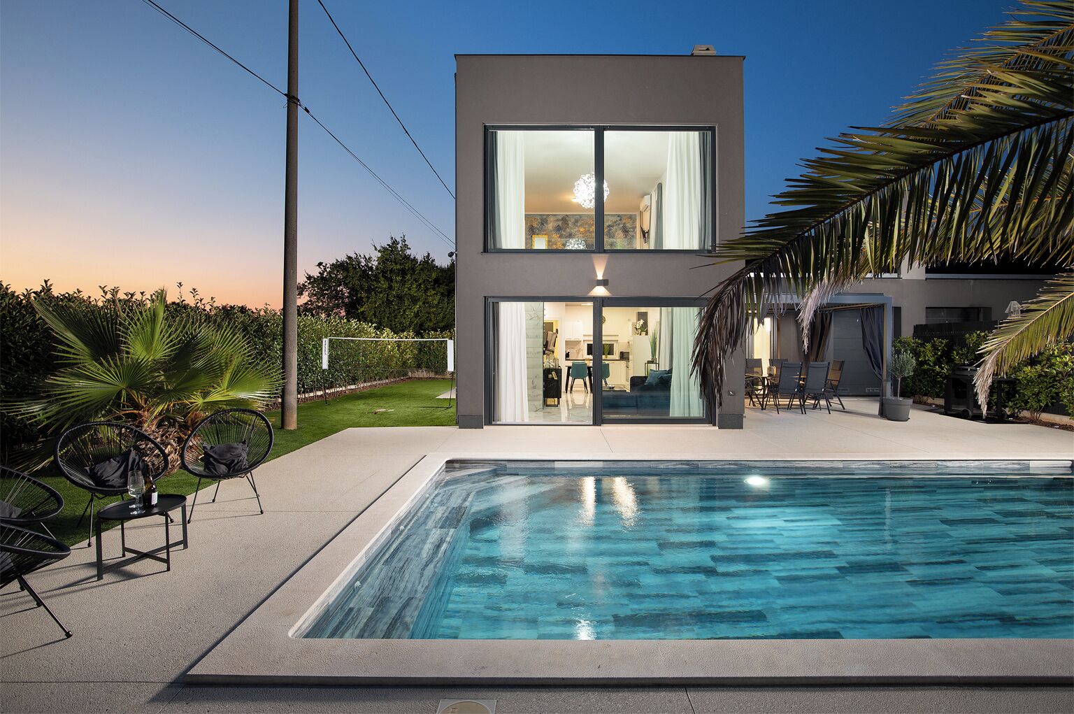A modern two-story house with a swimming pool, outdoor seating, and a well-maintained garden.