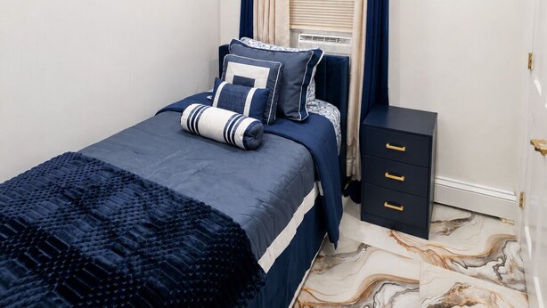 A bedroom with a bed, a bedside table, a wall-mounted shelf, and a window with curtains. - Royal 3-bedroom apartment/Wifi/15 min NYC/Bus stop 2 min/8 people (West New York)