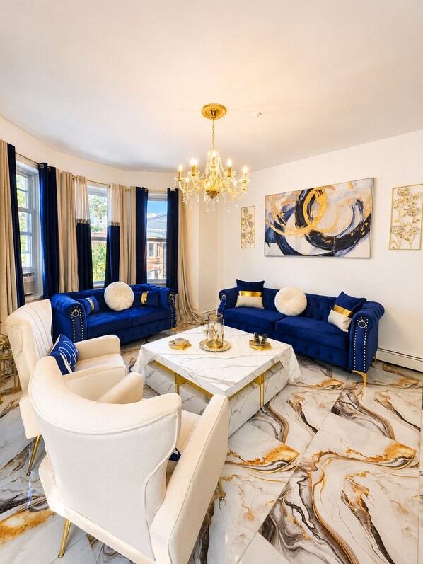Ein luxuriöses Wohnzimmer mit einer blauen Sofagarnitur, einem weißen Sessel und einem Boden mit Marmoroptik.