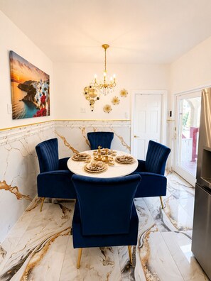 Ein Esszimmer mit einem runden Tisch, blauen Stühlen, einer Kronleuchter und einem Gemälde an der Wand.