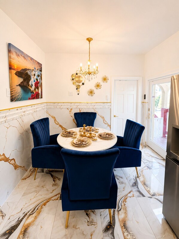 Uma sala de jantar com uma mesa redonda, cadeiras azuis, um lustre e um quadro na parede.