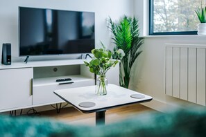A modern living room with a flat-screen TV, a small table with a vase of flowers, and a potted plant.