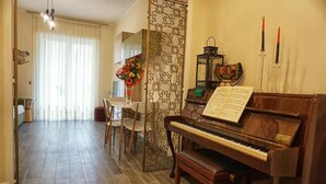 Ein Zimmer mit einem Klavier, einem Esstisch mit Stühlen, einem dekorativen Raumteiler und einem Fenster mit Vorhängen.