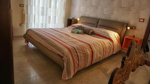 Ein Schlafzimmer mit einem großen Bett, einem Kopfteil, einem Nachttisch und einer Wand mit ornamentalem Wandpapier.