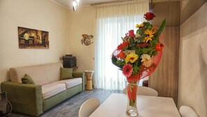Ein Wohnzimmer mit einer Couch, einem Esstisch und einer Blumenvase.