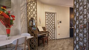 Ein Zimmer mit einem Klavier, einem Esstisch mit Stühlen und einem dekorativen Raumteiler mit Muster.