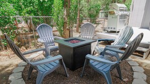 Une terrasse avec quatre fauteuils Adirondack, une table carrée et un barbecue.
