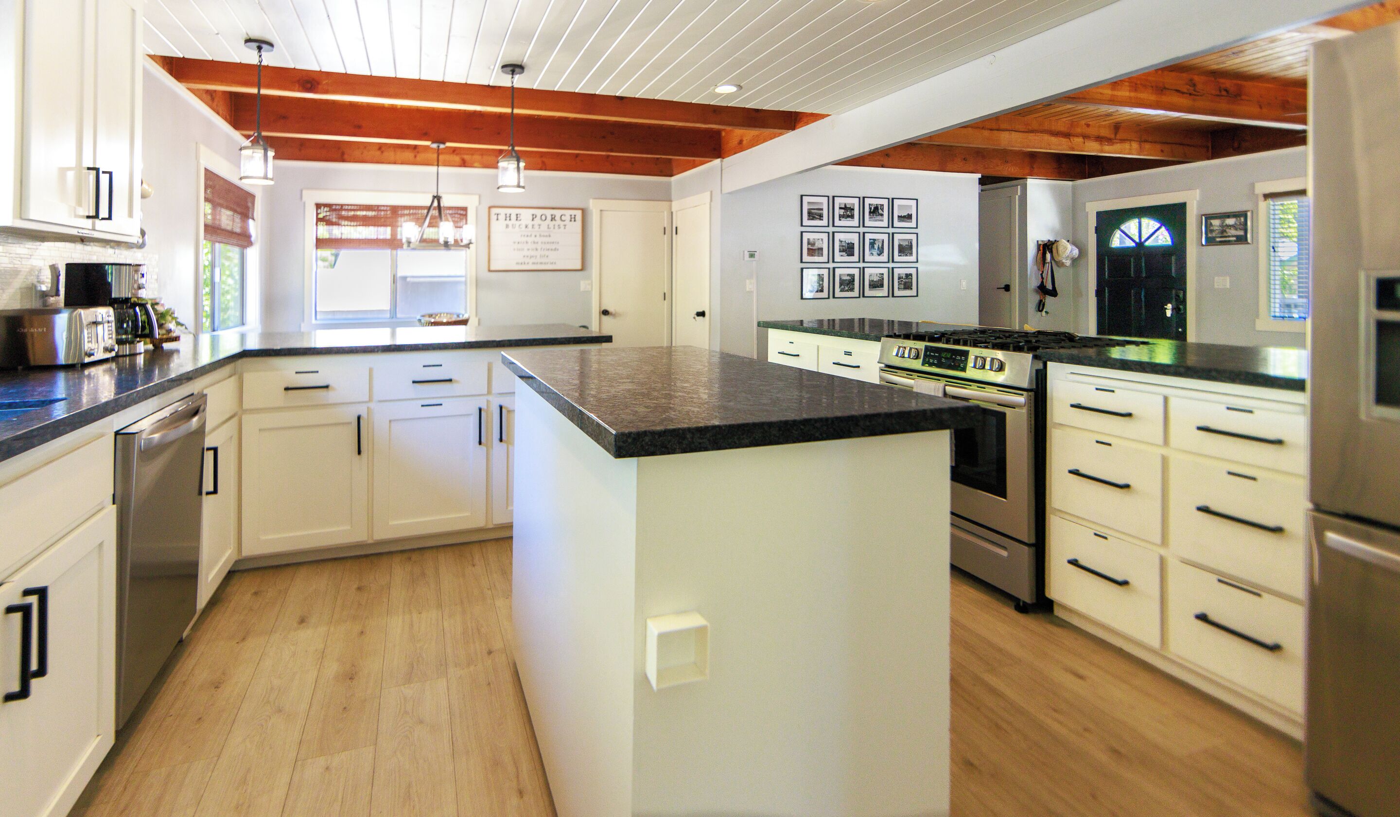 A modern kitchen with white cabinetry, a central island, stainless steel appliances, and wooden beams on the ceiling.