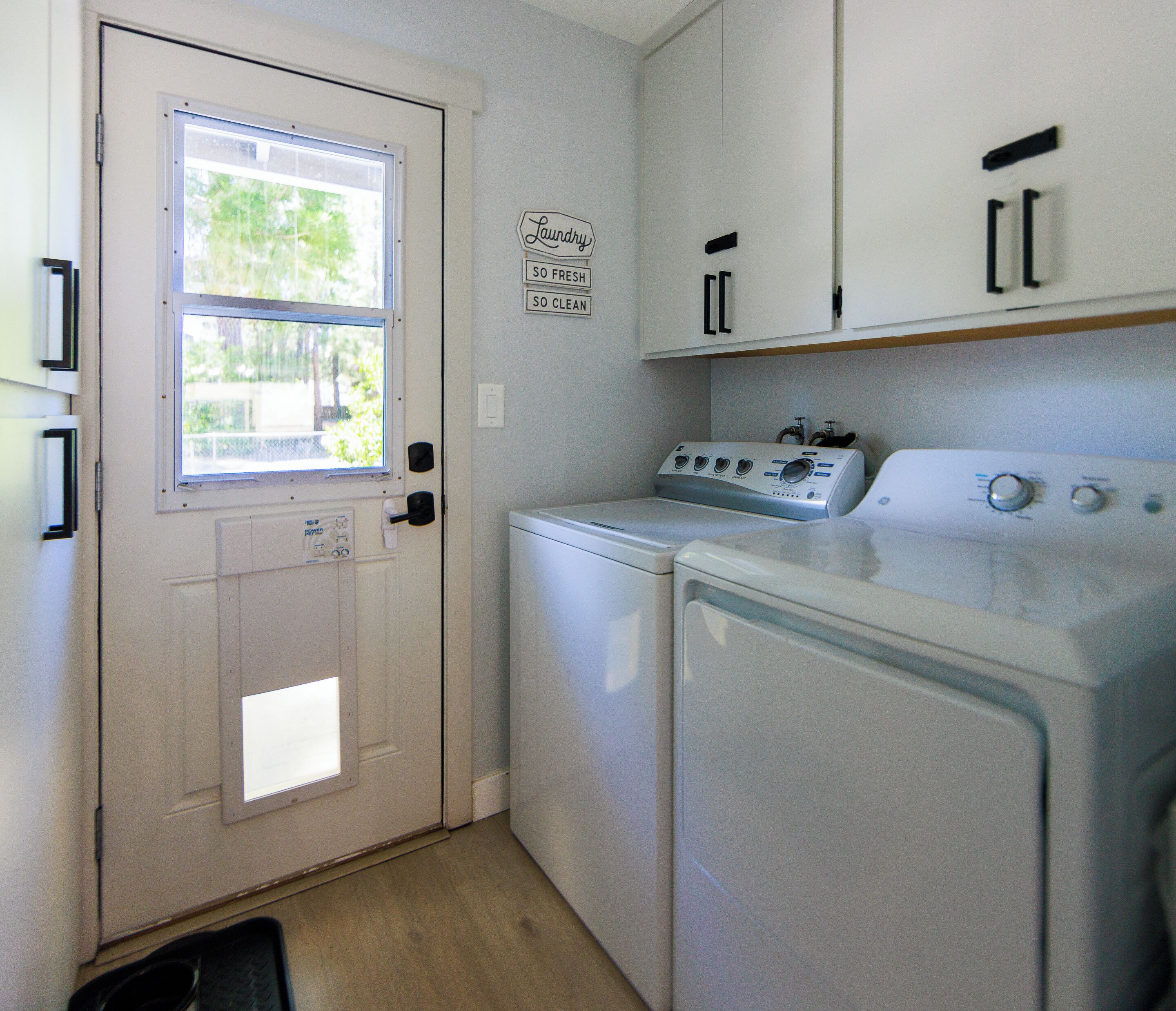 A laundry room with a door, a window, a wall-mounted sign, and two stacked washers and dryers.