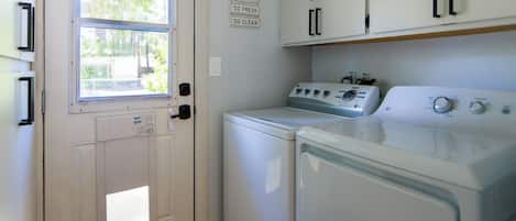 A laundry room with a door, a window, a wall-mounted sign, and two stacked washers and dryers.