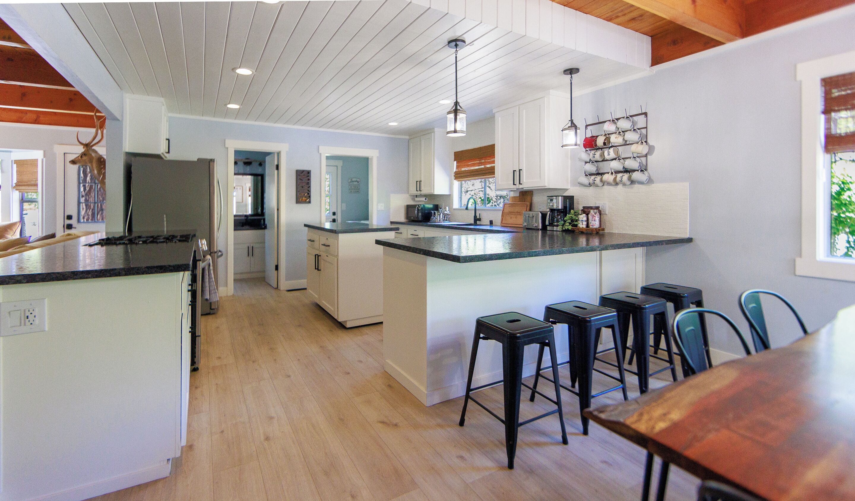 A kitchen with a central island, bar stools, and a hanging mug rack.