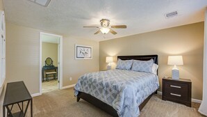 Ein Schlafzimmer mit Bett, Nachttischen, Deckenventilator und einer Tür zu einem anderen Raum.