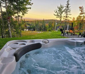 Un jacuzzi con vistas a un bosque y una cabaña al fondo.
