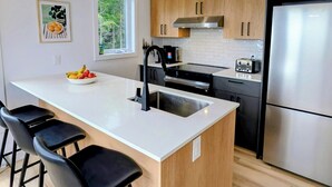 A modern kitchen with a central island, bar stools, stainless steel appliances, and wooden cabinets.