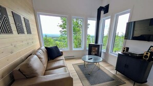 A modern living room with a leather sofa, a round coffee table, a black TV stand, and large windows offering a view of the outdoors.