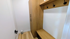 A room with a wooden bench, a white wall, and a wooden shelf with hooks.