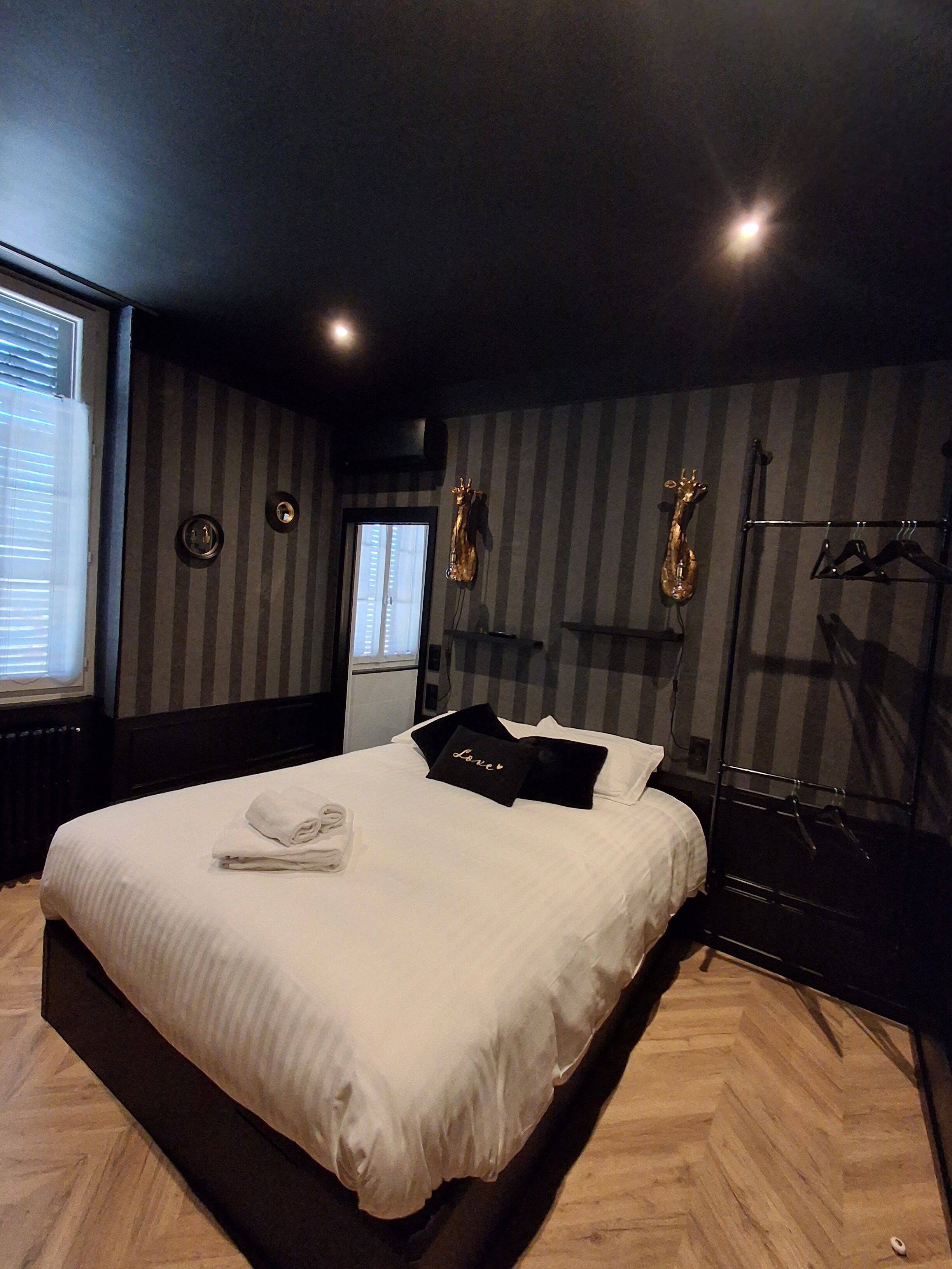 A modern hotel room with a large bed, a mirror, a wardrobe, and a window with blinds.
