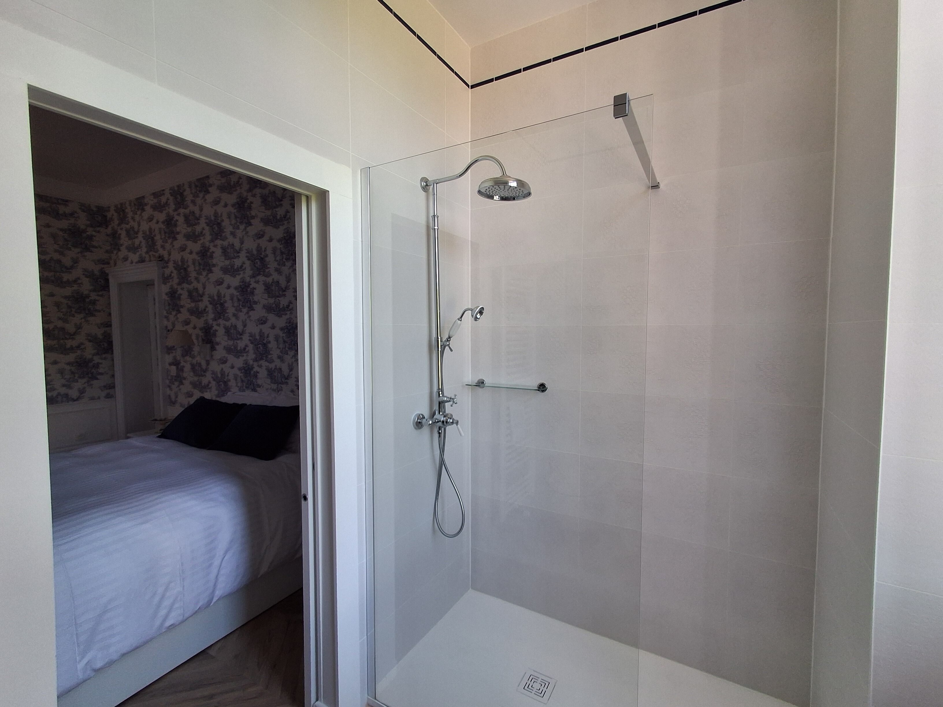 Una habitación con una cama, una ducha con puerta de vidrio y una pared con papel tapiz estampado.