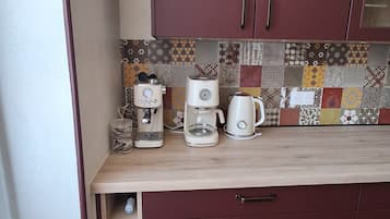 A kitchen with a coffee maker, a kettle, and a microwave on the counter. There are cabinets with handles and a tiled backsplash.