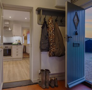 A room with a kitchen, a coat rack with a leopard print item, and a blue door. - The Woodhall Park Collection | Sleeps 20 (Hetford)