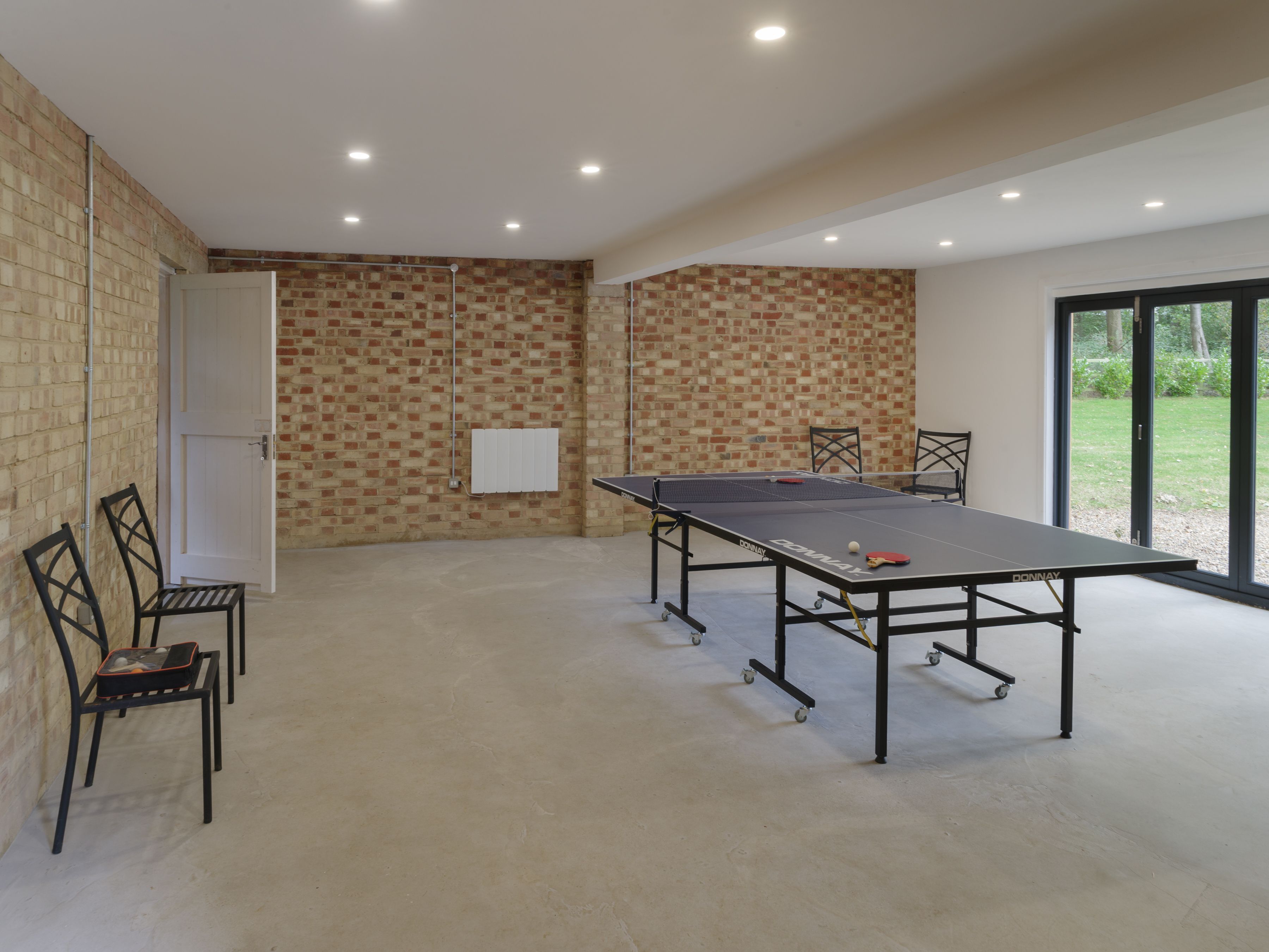A ping pong table in a room with a brick wall, a whiteboard, and a view through a glass door.