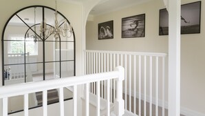 Una escalera con barandales blancos, un candelabro y obras de arte en la pared.