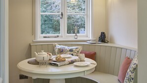A dining area with a round table, bench seating, a window with a view of trees, and a hanging light fixture. - Ware Lodge at Woodhall Park | Sleeps 3 (Hetford)