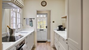 A kitchen with a sink, stove, and cabinets, a clock on the wall, and a door leading outside. - Ware Lodge at Woodhall Park | Sleeps 3 (Hetford)