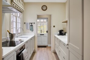 A kitchen with a sink, stove, and cabinets, a clock on the wall, and a door leading outside. - Ware Lodge at Woodhall Park | Sleeps 3 (Hetford)