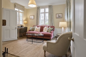 A living room with a sofa, armchairs, a coffee table, a lamp, a desk, and a window with curtains. - Ware Lodge at Woodhall Park | Sleeps 3 (Hetford)