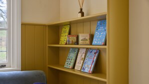 A bookshelf with children's books and a window with a view of trees. - Ware Lodge at Woodhall Park | Sleeps 3 (Hetford)