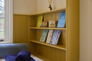 A bookshelf with children's books and a window with a view of trees. - Ware Lodge at Woodhall Park | Sleeps 3 (Hetford)