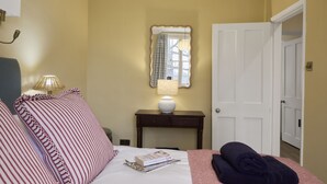 A hotel room with a bed, bedside lamps, a bedside table with a lamp, a mirror, and a door. - Ware Lodge at Woodhall Park | Sleeps 3 (Hetford)