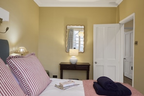 A hotel room with a bed, bedside lamps, a bedside table with a lamp, a mirror, and a door. - Ware Lodge at Woodhall Park | Sleeps 3 (Hetford)