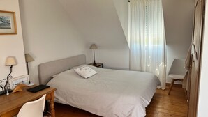 Een slaapkamer met een bed, een bureau, een stoel, een lamp en een raam met gordijnen.