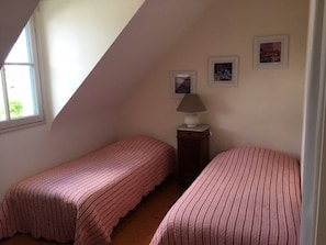 A bedroom with two single beds, a lamp, and framed pictures on the wall.