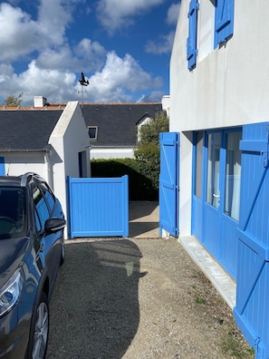 A residential property with a gravel driveway, a car parked on the left, and a blue gate leading to the house. - House for rent, 5 minutes from the beach, Samzun, Belle-Île-en-Mer (Locmaria)