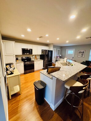 A modern kitchen with white cabinets, stainless steel appliances, a granite countertop, and a bar area with stools. - Family-Friendly Bradenton Retreat with Private Pool (Bradenton)