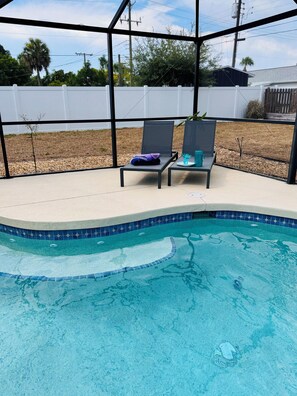 Ein Pool mit zwei Liegestühlen und einem Tisch, umgeben von einem weißen Zaun und Bäumen.