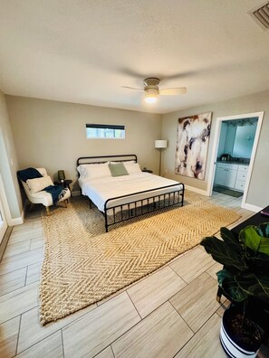 A bedroom with a bed, a chair, a floor lamp, a ceiling fan, a window, and a door leading to a bathroom. - Family-Friendly Bradenton Retreat with Private Pool (Bradenton)