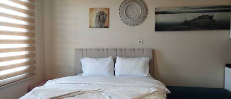A bedroom with a bed, a painting, a clock, and a wooden table.