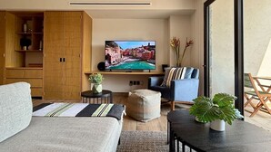 Un salon moderne avec un téléviseur à écran plat, un canapé, un fauteuil, une petite table et une plante en pot.