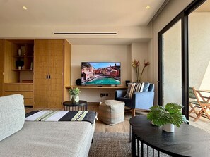 Ein modernes Wohnzimmer mit Flachbildfernseher, einer Couch, einem Sessel, einem kleinen Tisch und einem Blumentopf.