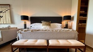 Une chambre d’hôtel comprenant un lit, deux lampes de chevet, un banc, un canapé et un mur orné d’un élément décoratif.