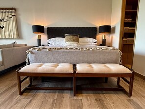 Ein Hotelzimmer mit einem Bett, zwei Nachttischlampen, einer Bank, einem Sofa und einer Wand mit einem dekorativen Element.