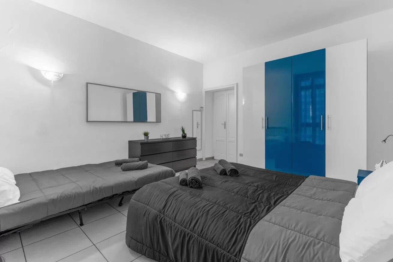 Une chambre moderne avec deux lits simples, une commode, un miroir et une armoire bleue.