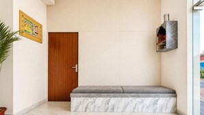 A hallway with a wooden door, a bench with a marble base, and a shelf with books and a decorative item. - Collection O Salasar Balaji Temple (Sujangarh)