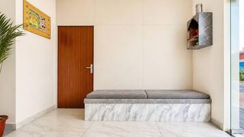 A hallway with a wooden door, a bench with a marble base, and a shelf with books and a decorative item.