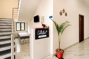 A hotel reception area with a marble staircase, a reception desk, a potted plant, and a wall-mounted sign. - Collection O Salasar Balaji Temple (Sujangarh)