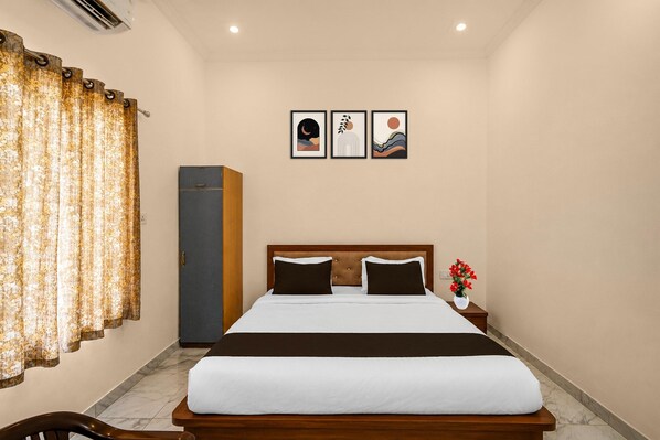 A hotel room with a bed, a wardrobe, a nightstand with a vase of flowers, and two framed pictures on the wall.